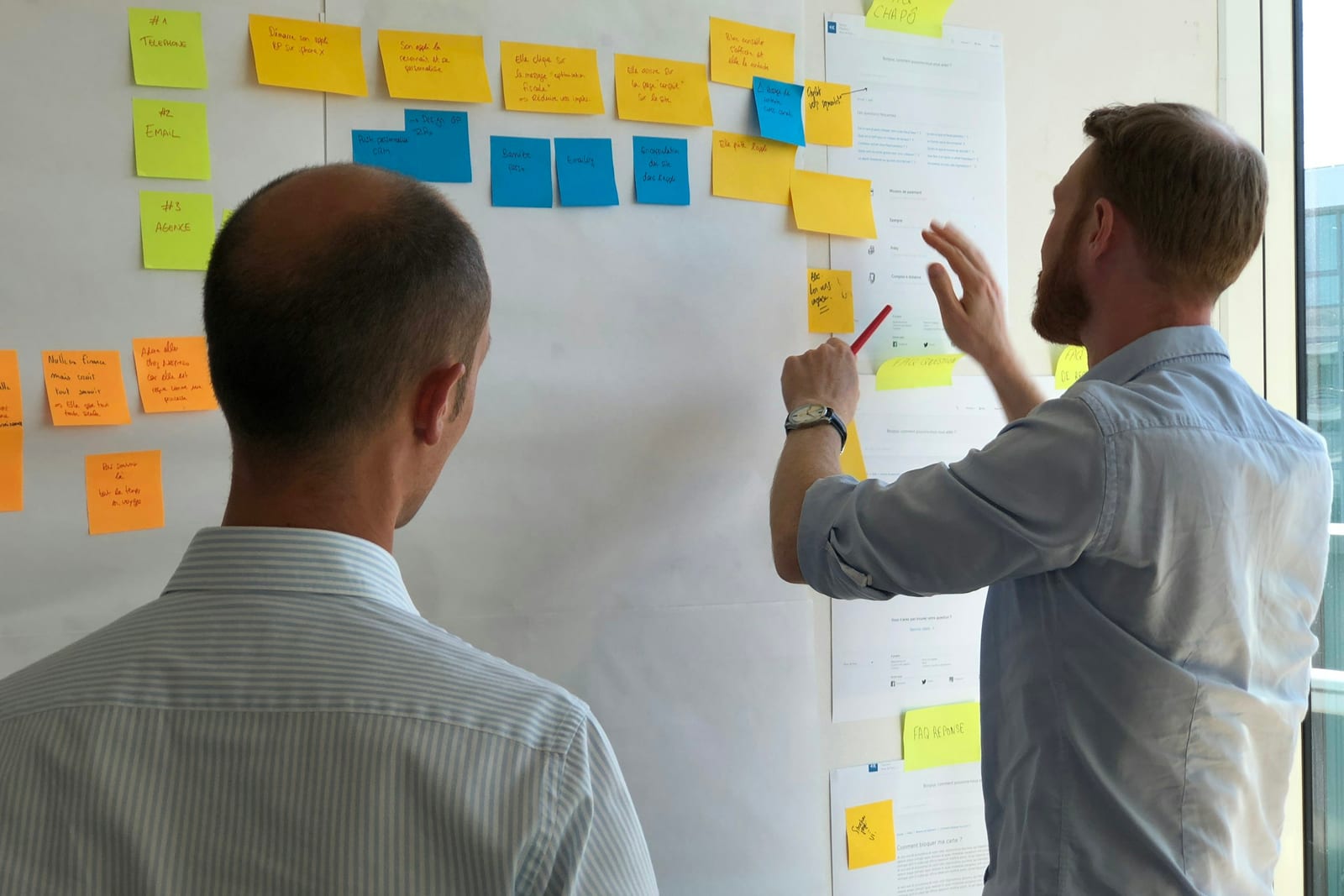 Two colleagues planning with sticky notes on a bright wall, seen from behind